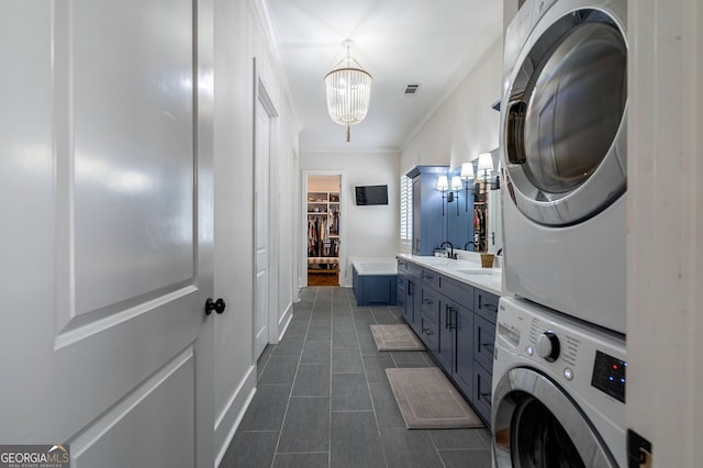 washroom featuring stacked washing maching and dryer, dark tile patterned floors, crown molding, sink, and an inviting chandelier