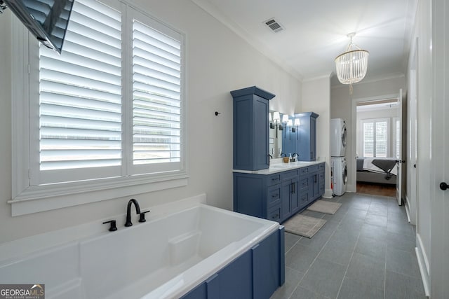 bathroom featuring vanity, stacked washer / drying machine, ornamental molding, a notable chandelier, and a tub