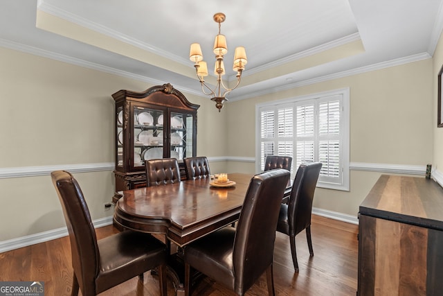 dining area featuring a raised ceiling, dark wood-type flooring, a chandelier, and ornamental molding