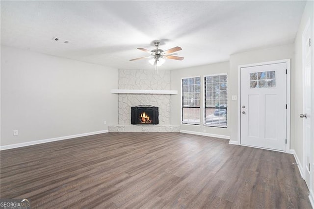 unfurnished living room featuring ceiling fan, a stone fireplace, and dark wood-type flooring