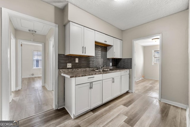 kitchen featuring white cabinets, sink, a textured ceiling, tasteful backsplash, and light hardwood / wood-style floors