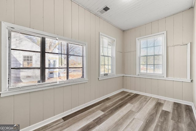 empty room with light hardwood / wood-style flooring, a wealth of natural light, and wood walls