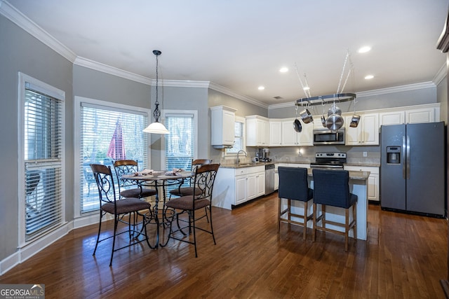 kitchen featuring white cabinetry, stainless steel appliances, crown molding, pendant lighting, and a kitchen island