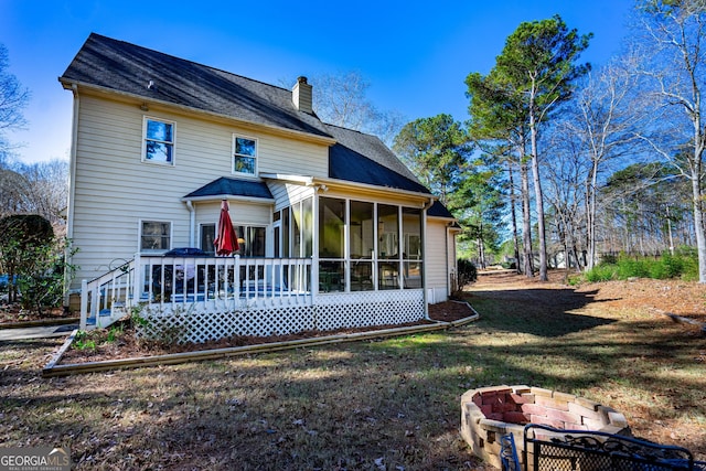 back of house featuring a fire pit, a lawn, a deck, and a sunroom