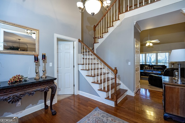 stairs featuring hardwood / wood-style flooring, ceiling fan with notable chandelier, and a towering ceiling