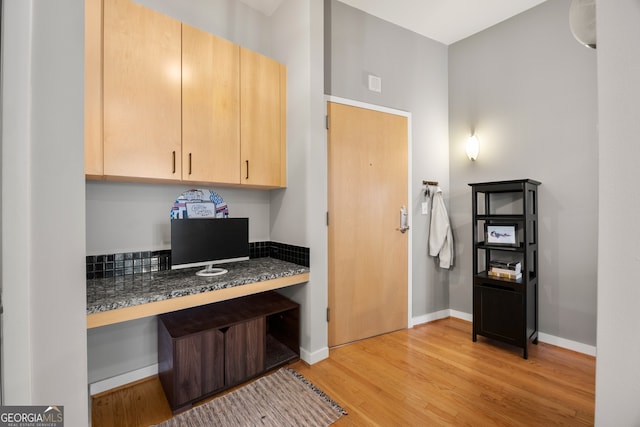 interior space with dark stone countertops, light brown cabinets, built in desk, and light hardwood / wood-style flooring