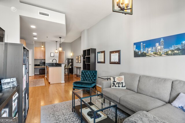 living room with light hardwood / wood-style floors, sink, a high ceiling, and an inviting chandelier