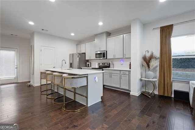 kitchen with dark hardwood / wood-style flooring, a wealth of natural light, stainless steel appliances, a breakfast bar area, and an island with sink