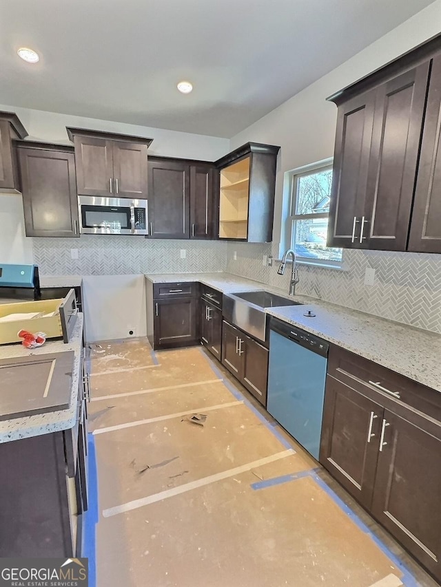 kitchen with decorative backsplash, appliances with stainless steel finishes, light stone counters, dark brown cabinetry, and sink