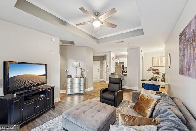 living room with a raised ceiling, ceiling fan, hardwood / wood-style floors, and ornamental molding