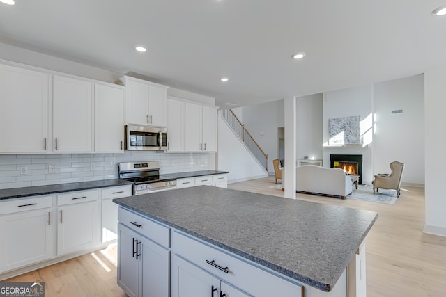240 Good Hope Preserve, Good Hope, GA 30641 - kitchen with stainless steel appliances, a kitchen island, a warm lit fireplace, backsplash, and white cabinetry