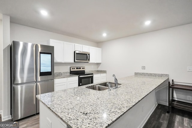 kitchen with kitchen peninsula, appliances with stainless steel finishes, light stone countertops, sink, and white cabinets