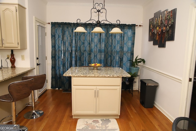 kitchen featuring light stone countertops, crown molding, pendant lighting, light hardwood / wood-style floors, and cream cabinetry