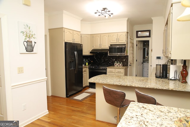 kitchen featuring light stone counters, backsplash, kitchen peninsula, a breakfast bar, and black appliances