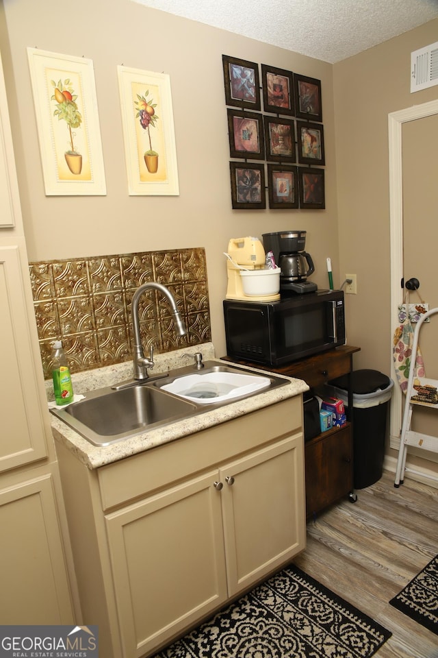 kitchen with cream cabinets, sink, a textured ceiling, and light wood-type flooring