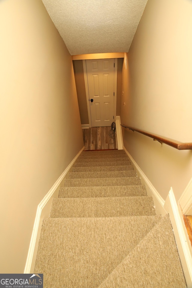 staircase featuring a textured ceiling and carpet floors