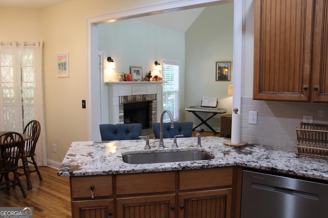 kitchen with backsplash, sink, stainless steel dishwasher, a fireplace, and light stone counters