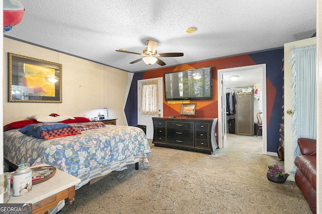 carpeted bedroom with a walk in closet, ceiling fan, a closet, and a textured ceiling