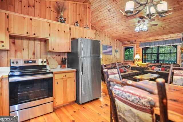 kitchen featuring appliances with stainless steel finishes, ceiling fan with notable chandelier, vaulted ceiling, light hardwood / wood-style flooring, and wood walls