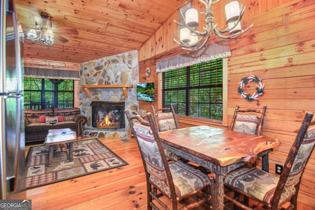 dining space featuring wooden ceiling, wood walls, wood-type flooring, a fireplace, and ceiling fan with notable chandelier