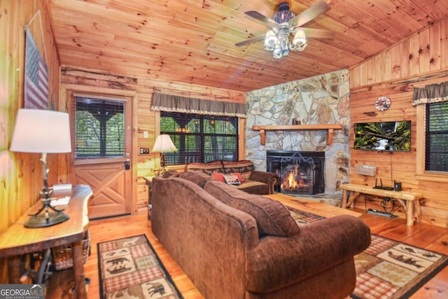 living room with a stone fireplace, wooden walls, ceiling fan, and light hardwood / wood-style floors