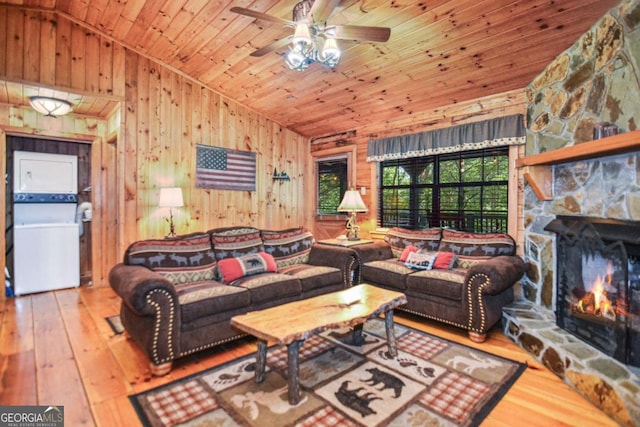 living room with lofted ceiling, stacked washer and dryer, wooden walls, ceiling fan, and wood ceiling