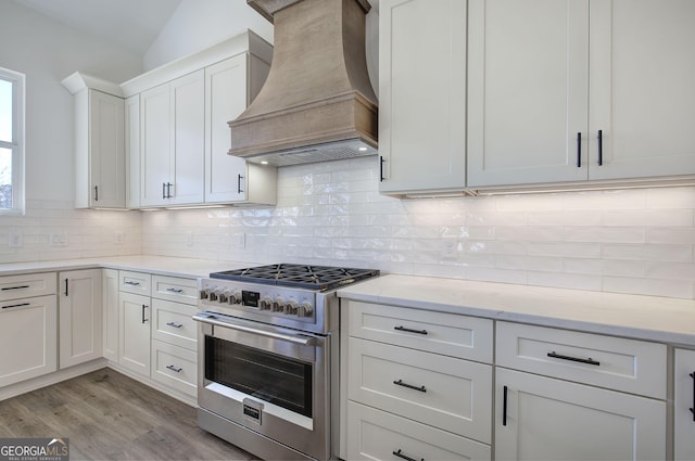 kitchen featuring high end range, backsplash, premium range hood, and white cabinetry