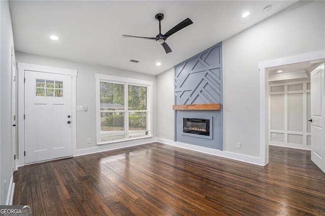 unfurnished living room featuring ceiling fan, plenty of natural light, a large fireplace, and dark hardwood / wood-style floors