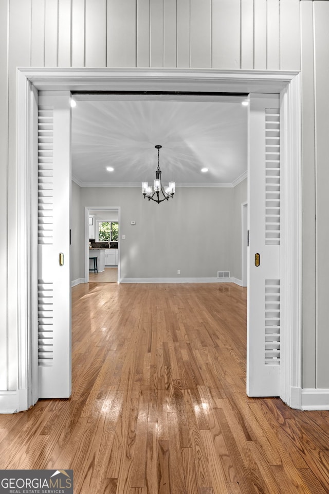 unfurnished dining area with a chandelier, light wood-type flooring, and ornamental molding