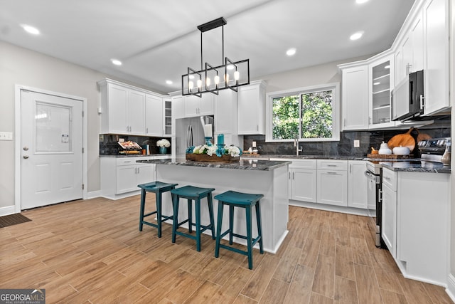 kitchen featuring white cabinetry, a center island, stainless steel appliances, dark stone counters, and a breakfast bar