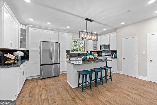 kitchen with decorative backsplash, stainless steel appliances, white cabinetry, and dark stone countertops