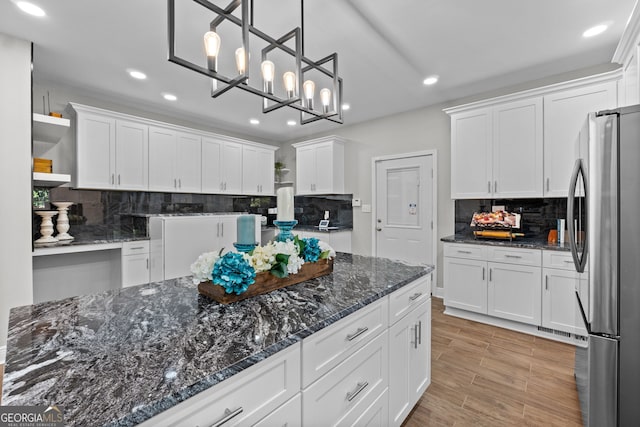 kitchen with white cabinetry, hanging light fixtures, tasteful backsplash, stainless steel fridge, and dark stone counters