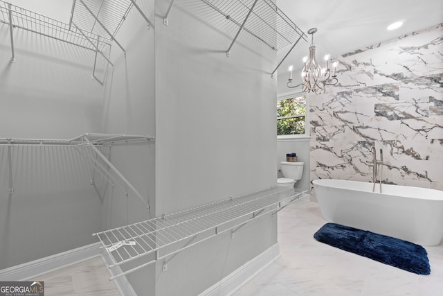 bathroom with a tub to relax in, an inviting chandelier, and toilet