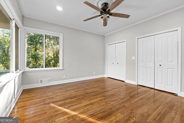 unfurnished bedroom featuring ceiling fan, crown molding, two closets, and hardwood / wood-style flooring