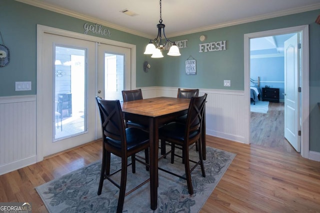 dining room with light hardwood / wood-style floors, french doors, crown molding, and an inviting chandelier