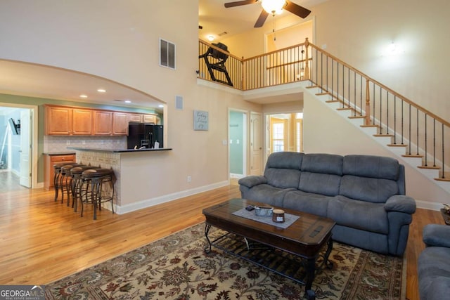 living room with ceiling fan, light hardwood / wood-style flooring, and a towering ceiling