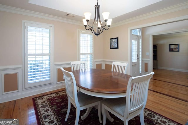 dining room with hardwood / wood-style flooring, plenty of natural light, ornamental molding, and a notable chandelier