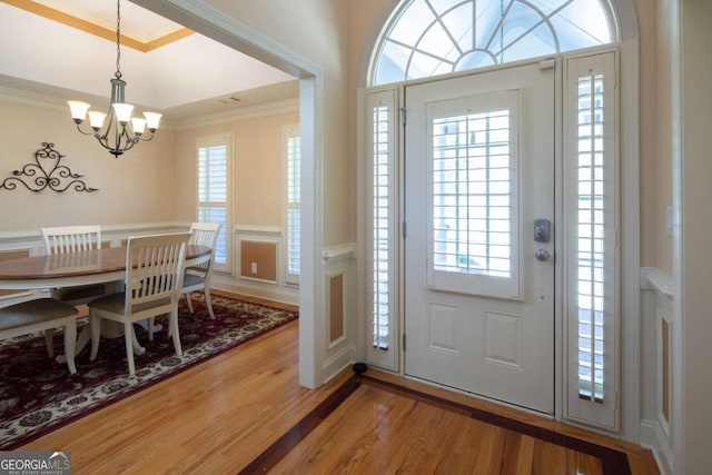 foyer entrance with hardwood / wood-style flooring, ornamental molding, and a notable chandelier