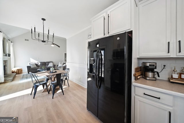 kitchen with light wood-type flooring, backsplash, black refrigerator with ice dispenser, white cabinetry, and hanging light fixtures