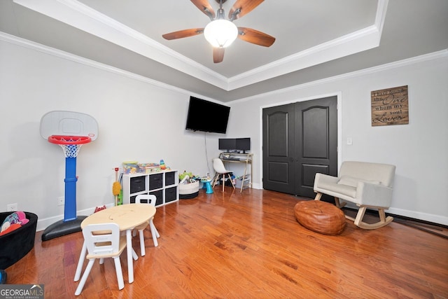 recreation room with a tray ceiling, crown molding, ceiling fan, and hardwood / wood-style flooring