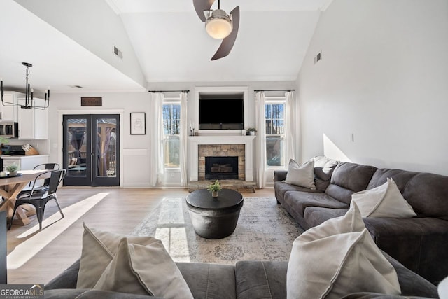 living room featuring ceiling fan with notable chandelier, light hardwood / wood-style floors, a fireplace, and high vaulted ceiling