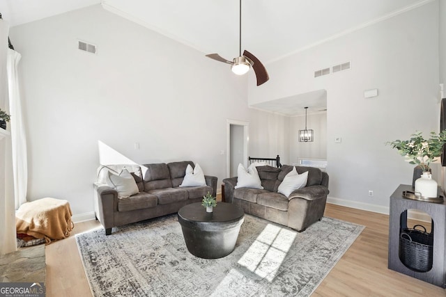 living room with light hardwood / wood-style flooring, high vaulted ceiling, ceiling fan with notable chandelier, and ornamental molding