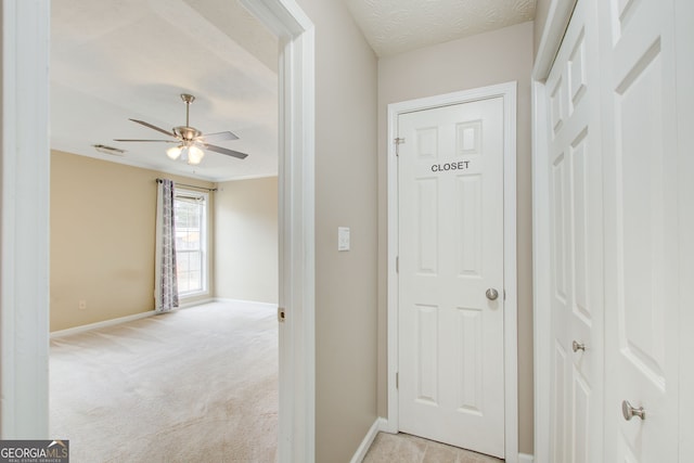 hallway featuring light colored carpet and a textured ceiling