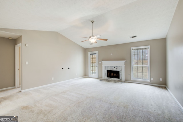 unfurnished living room with ceiling fan, vaulted ceiling, a high end fireplace, and light carpet