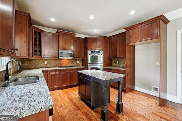 kitchen with light stone countertops, sink, appliances with stainless steel finishes, a kitchen island, and ornamental molding