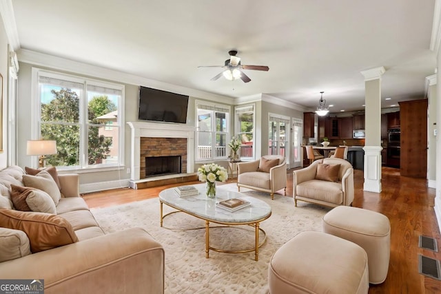 living room featuring a stone fireplace, crown molding, light hardwood / wood-style flooring, and ceiling fan with notable chandelier