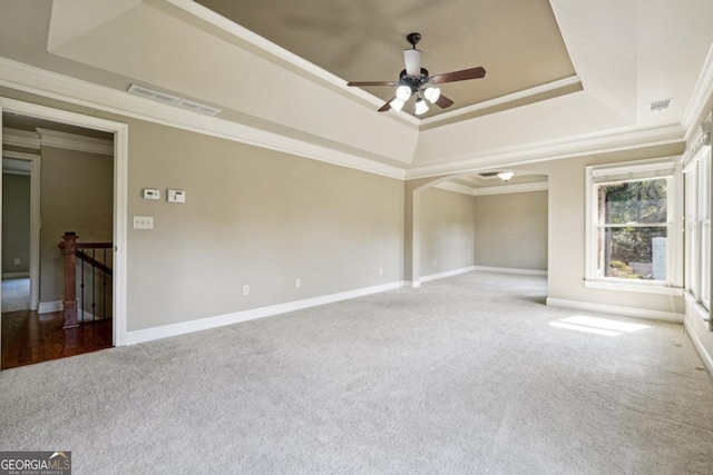 empty room with carpet flooring, ceiling fan, ornamental molding, and a tray ceiling