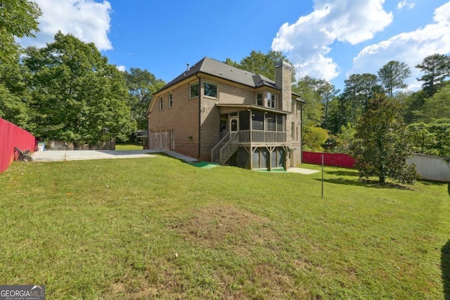 rear view of property with a yard, a garage, and a sunroom