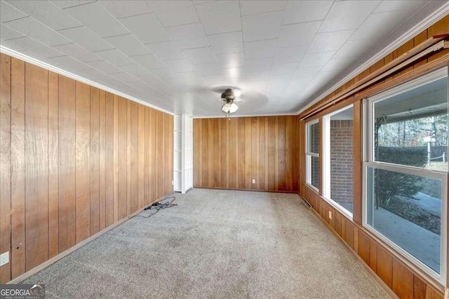 carpeted empty room featuring ceiling fan, crown molding, and wood walls