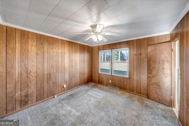 unfurnished room featuring ceiling fan, ornamental molding, carpet floors, and wooden walls